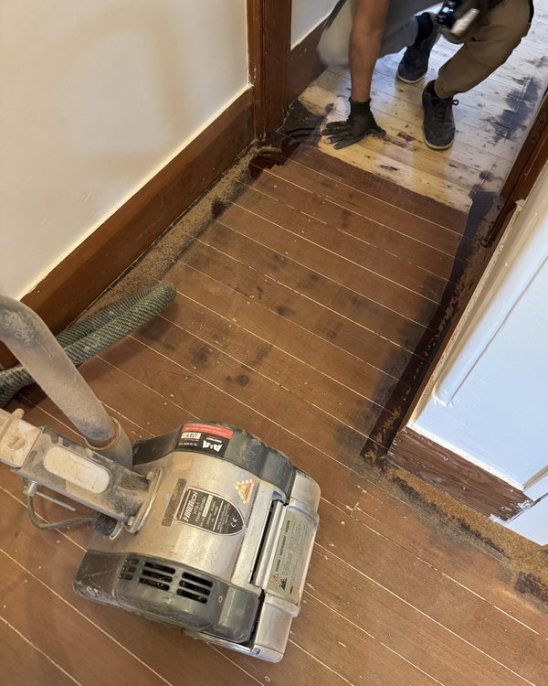 A floor part-sanded, showing raw timber against the old dark finish