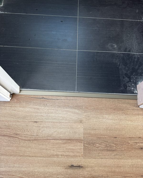 A transition strip between dark floor tiles and new timber flooring