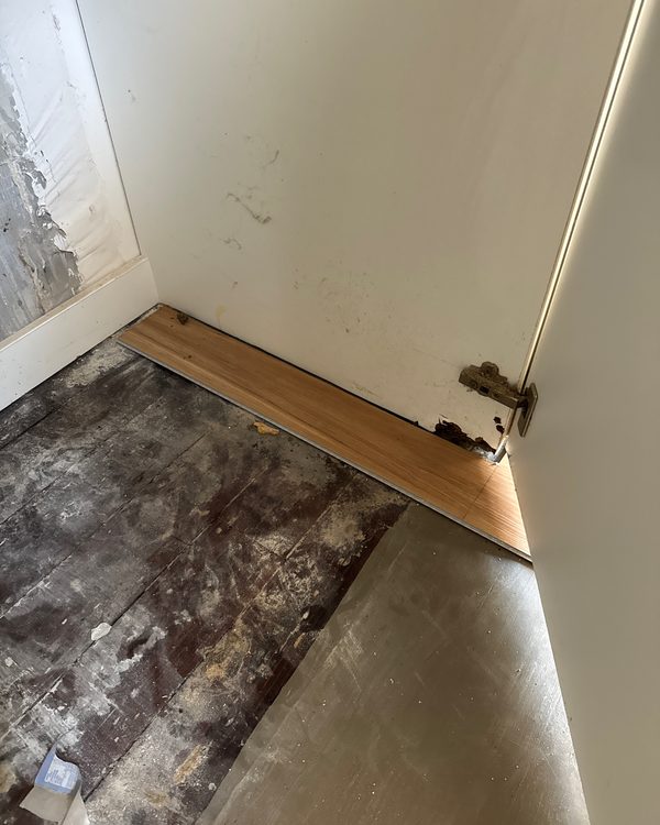 A new board set against old damaged floorboards during a repair