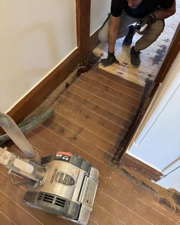 Old dark-stained floorboards being sanded back to raw timber